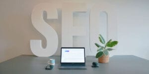 SEO spelt in large letters on a wall, pictured behind a laptop computer.