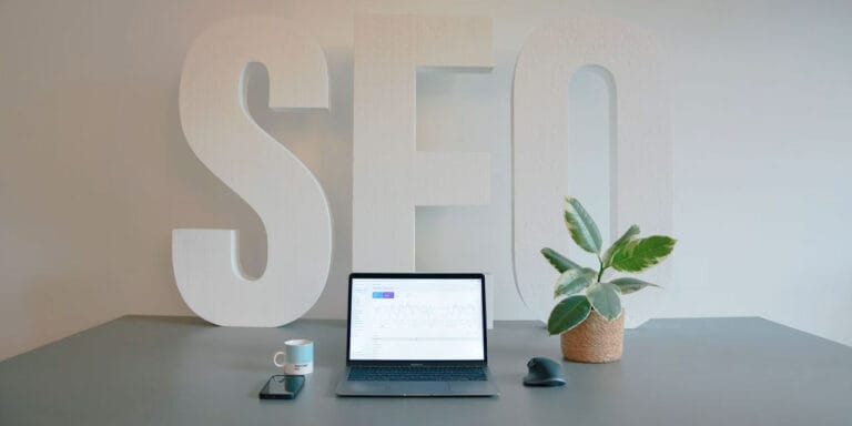 SEO spelt in large letters on a wall, pictured behind a laptop computer.