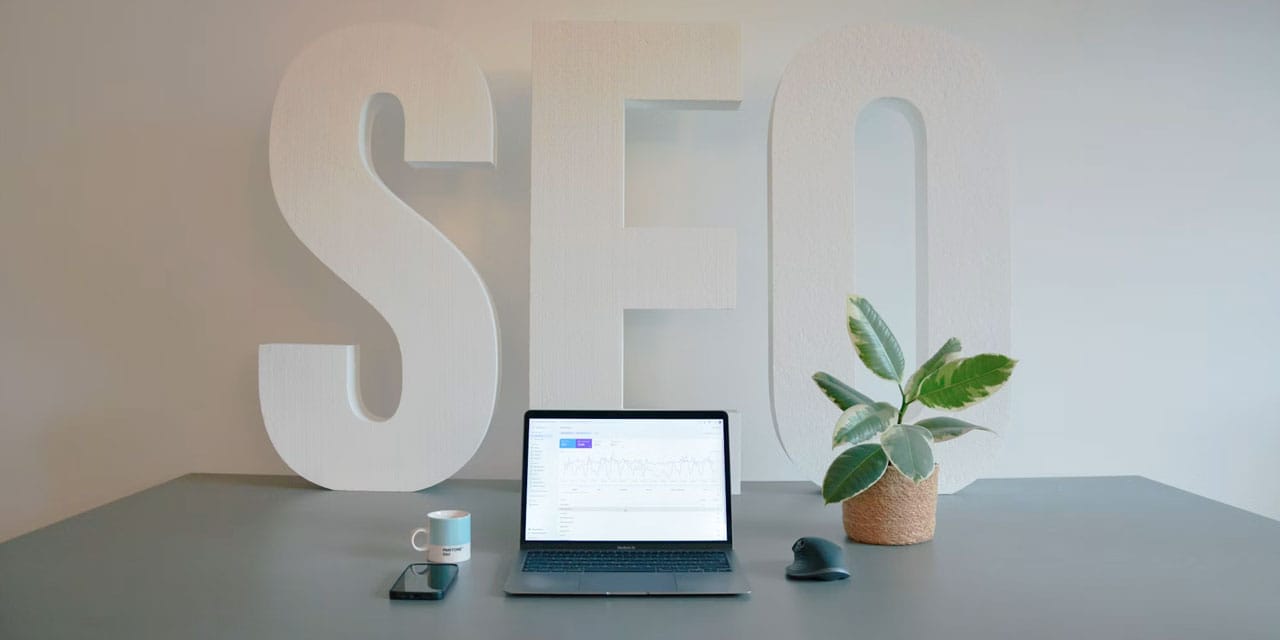 SEO spelt in large letters on a wall, pictured behind a laptop computer.