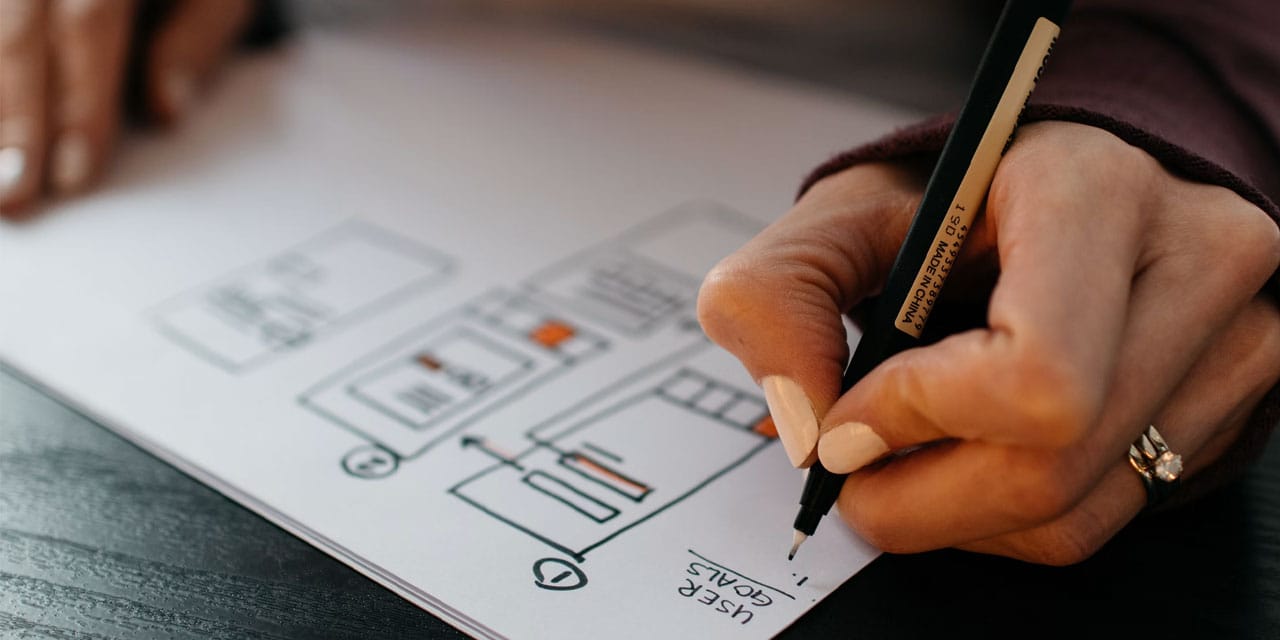 A picture of a hand holding a pen, drawing web design blocks