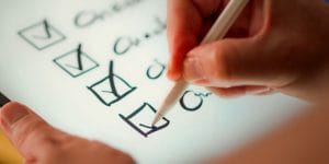 Close up of a hand holding a pen, ticking off items on a checklist.